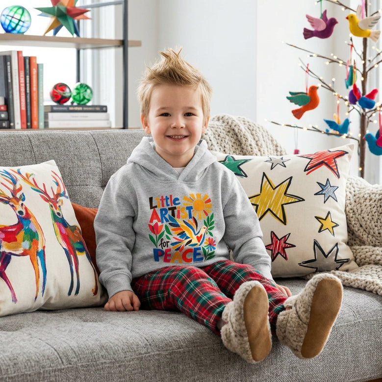 A toddler wears a gray hoodie with a festive design and the words "Little Artist for Peace"