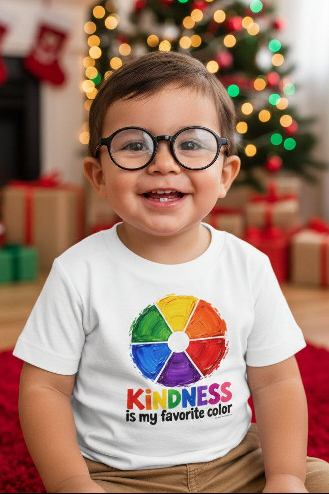 A white short-sleeve T-shirt on a toddler  wearing glasses. The shirt has a colorful rainbow wheel graphic above the text 'KINDNESS is my favorite color.'