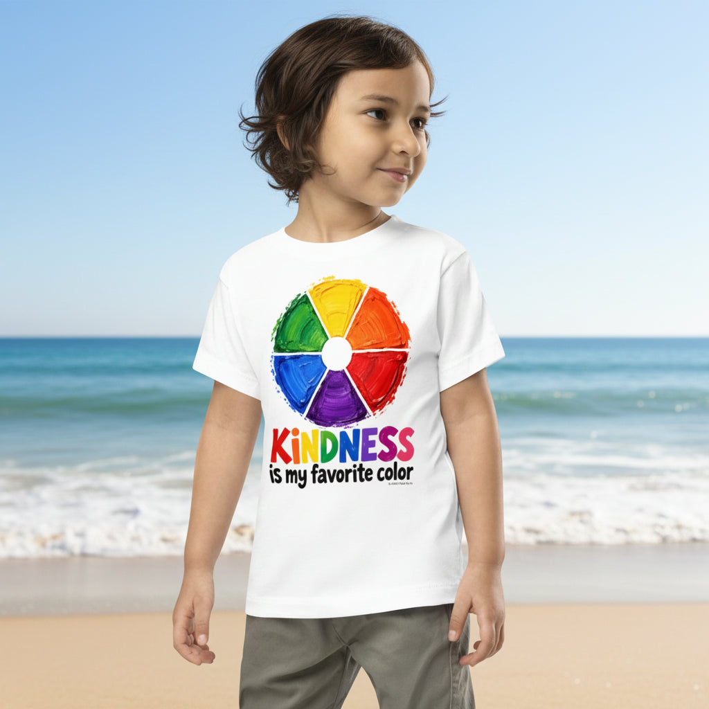 A child wearing a white graphic T-shirt and a beige knit beanie, standing against a plain white background. The shirt features a colorful paint-wheel style graphic with the text 'KINDNESS is my favorite color' printed below it.
