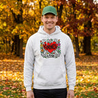 A man wearing a light gray pullover hoodie with a colorful graphic on the chest. The graphic features a red heart with the word 'Kindness' inside, surrounded by floral and decorative elements with the text 'Kindness IS FREE' below it.