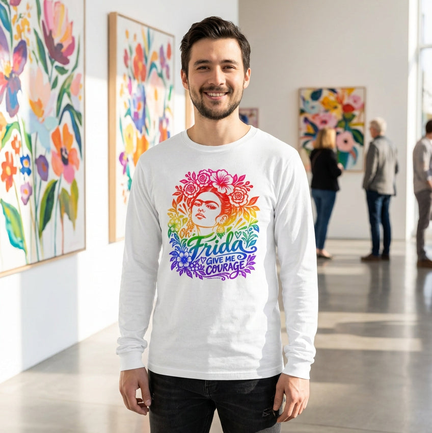 A man wearing a white long-sleeve t-shirt with a colorful graphic of Frida Kahlo's face surrounded by flowers and the text 'Oh Frida GIVE ME COURAGE' in a rainbow gradient stands in a well lit art museum with large flower paintings